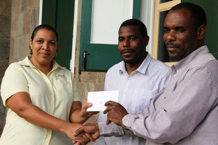 Support Coordinator Pink Lilly Cancer Care Group Ms. Tracy Parris (l) receiving a donation from President of the St. Georges Development and Enhancement Committee Mr. Collin Dore (r) and group member Mr. Devon Liburd (middle) on behalf of their group and the community for fellow villager Ms. Rubylette Chapman